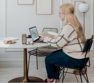 woman in white long sleeve shirt sitting on chair in front of microsoft surface laptop computer